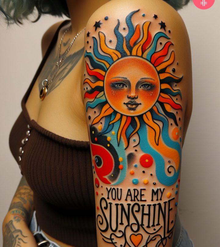 A 'you are my sunshine' tattoo on the upper arm of a woman
