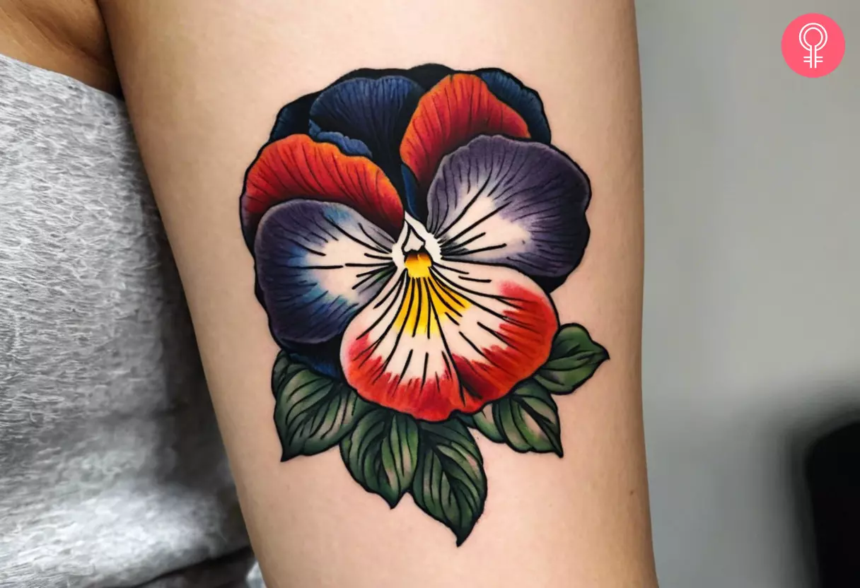 A vibrant and traditional pansy tattoo with green leaves on the upper arm