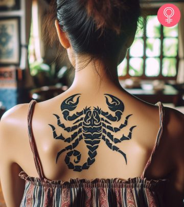 A tribal scorpion tattoo on a woman’s upper back