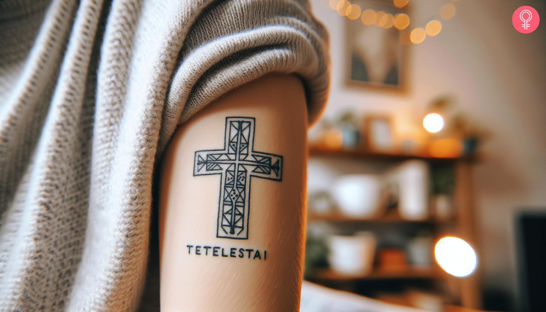 A Tetelestai cross tattoo on a woman's upper arm