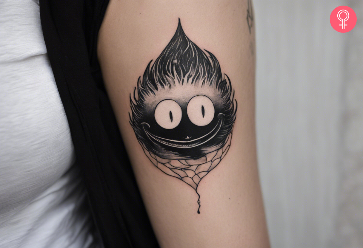 A black and white Calcifer tattoo on the inner upper arm