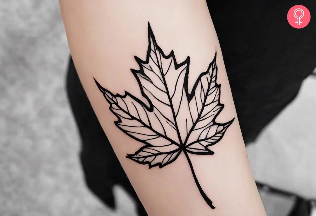 A black outline maple leaf tattoo on a woman’s forearm