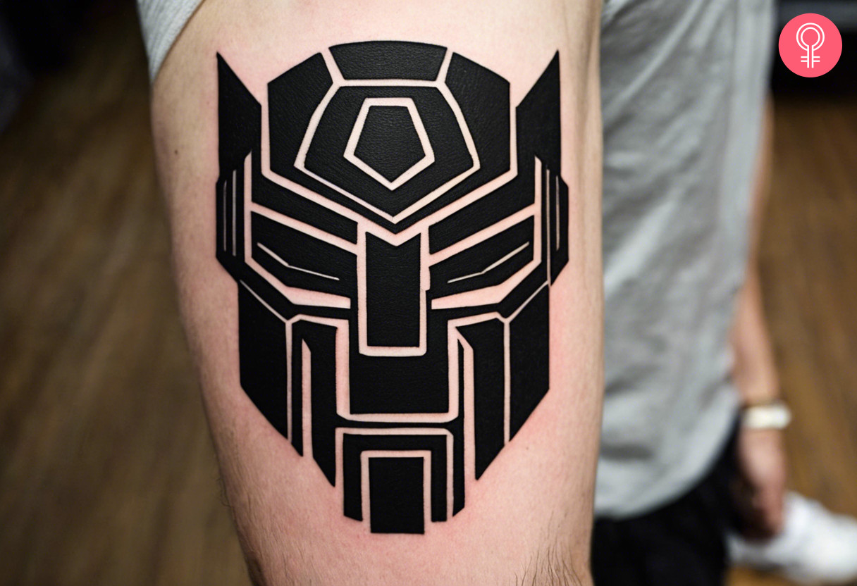 A bold black ink tattoo of the autobot symbol on the upper arm