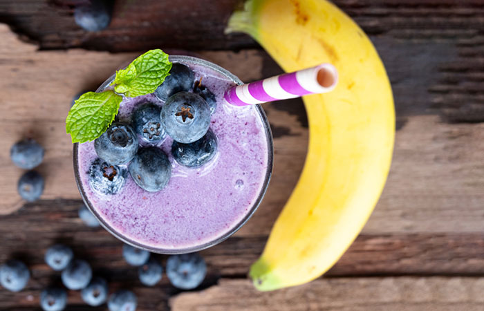 Um copo de shake de proteína caseiro de mirtilo, manteiga de amêndoa e banana na mesa