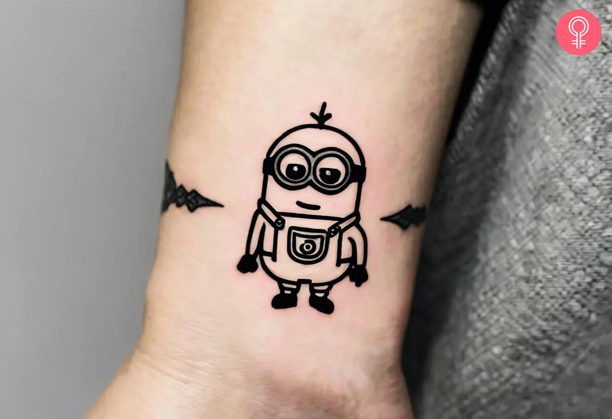 A minimalist minion tattoo on the wrist of a woman