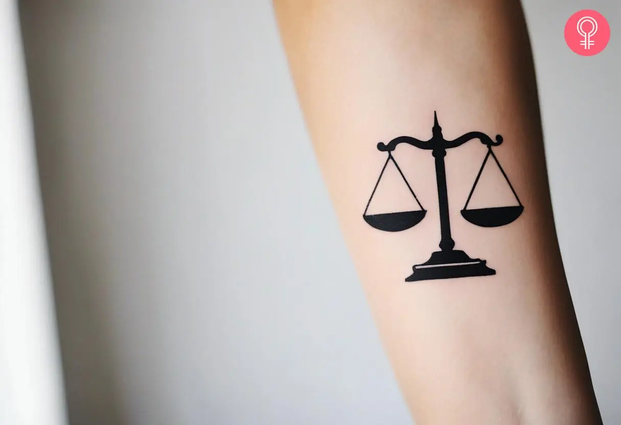 A minimalist scales of justice tattoo on the forearm of a woman