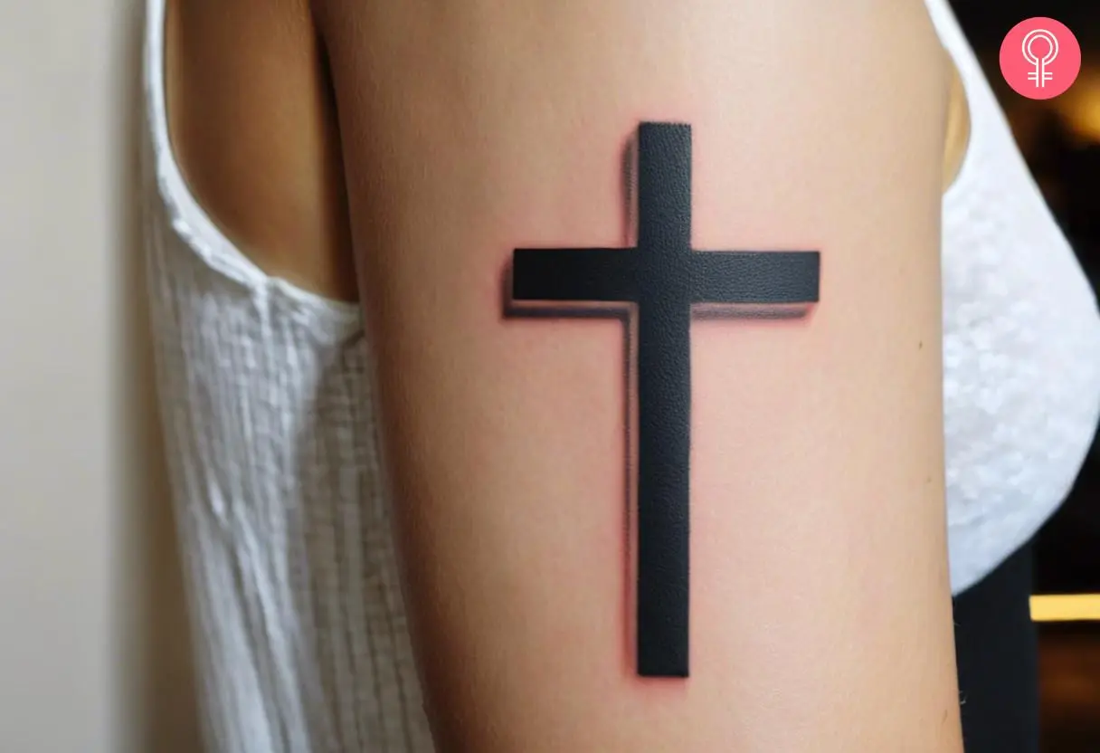 A shadow cross tattoo on a woman’s upper arm