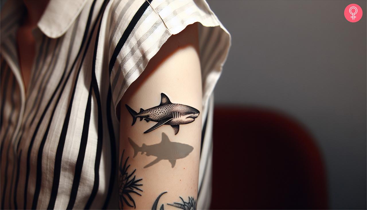 A shark with a shadow tattoo on a woman’s upper arm