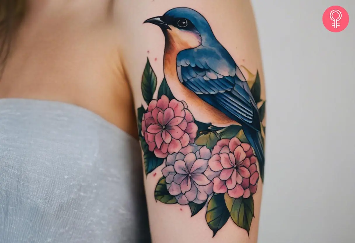 A tattoo of hydrangea and a bird on the upper arm of a woman