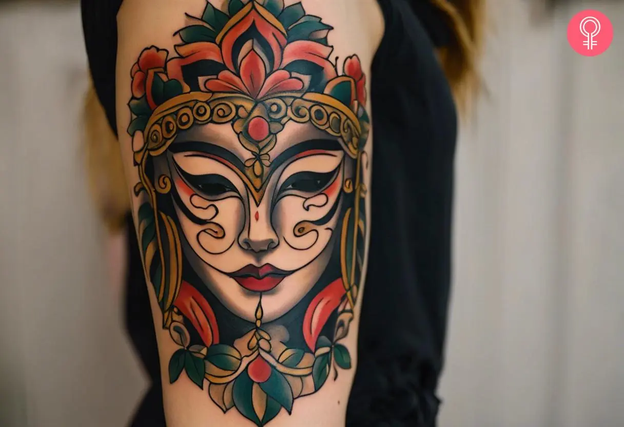 A traditional drama mask tattoo on the upper arm