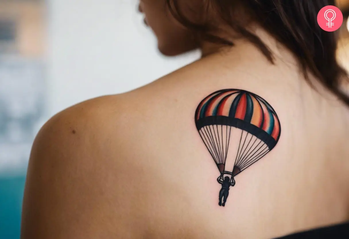 A woman with a colored skydiving tiny parachute tattoo on her upper back