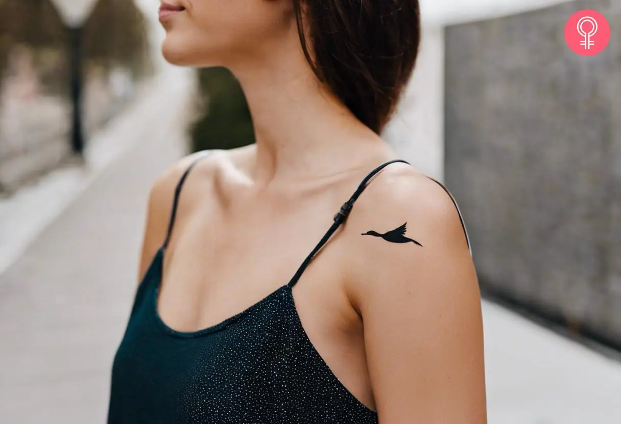 A woman with a minimalist goose tattoo on her shoulder cap