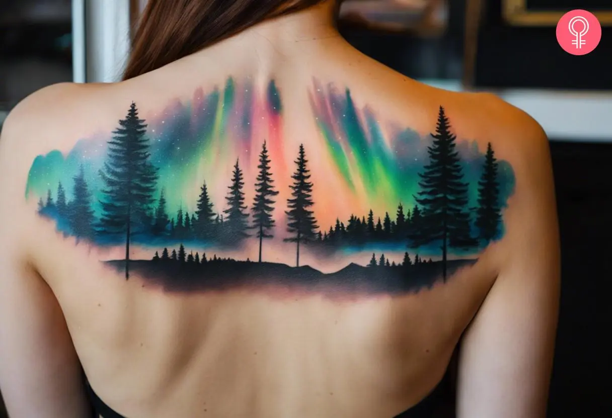 A woman with vibrant aurora borealis and pine trees tattoo on her upper back