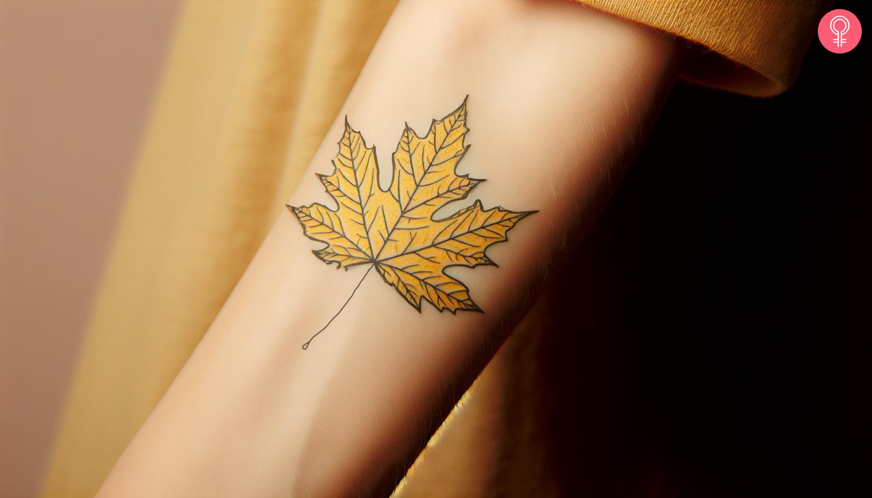 A yellow sugar maple leaf tattoo on a woman's forearm