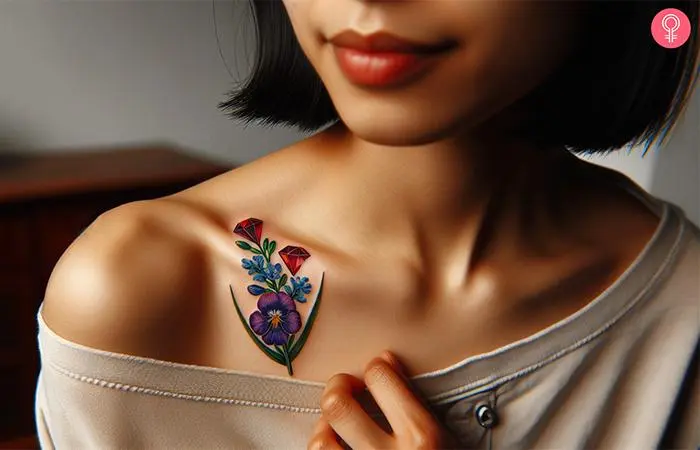 A birthstone gem tattoo with rubies and larkspur flowers on the collarbone of a woman