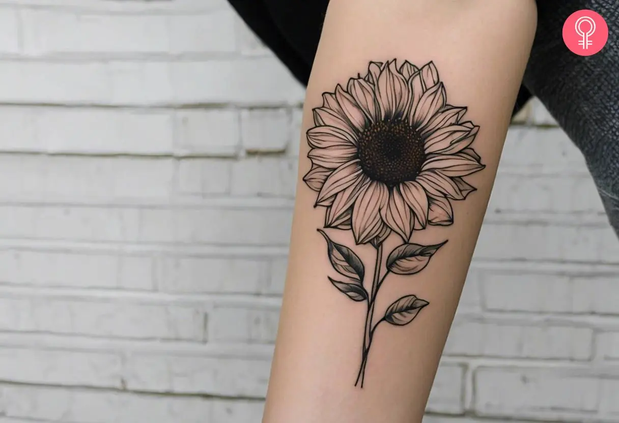 A black outline of a sunflower tattoo on the forearm of a woman