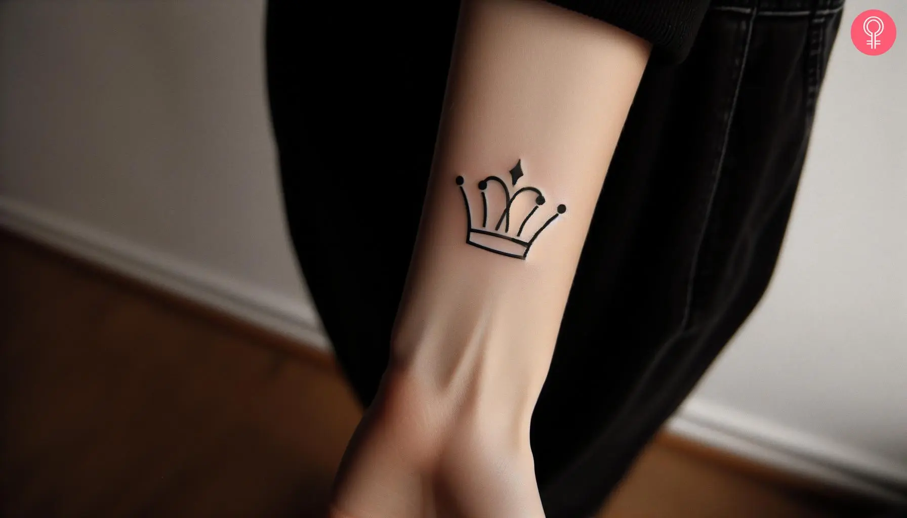 A minimalist black ink crown tattoo on the arm of a woman