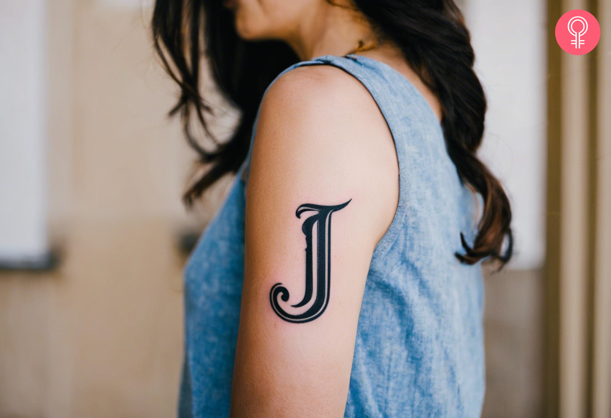 Black and bold J letter tattoo on the upper arm of a woman