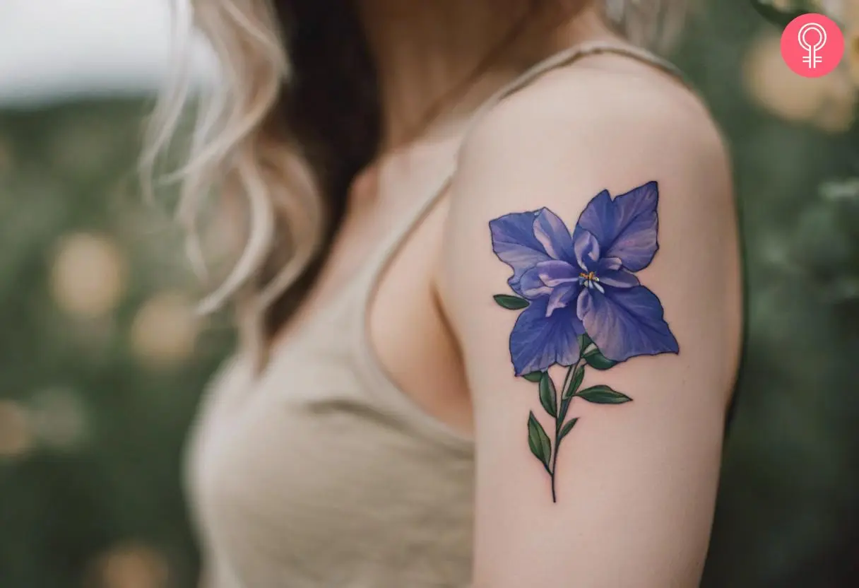 Blue larkspur flower tattoo on a woman’s upper arm