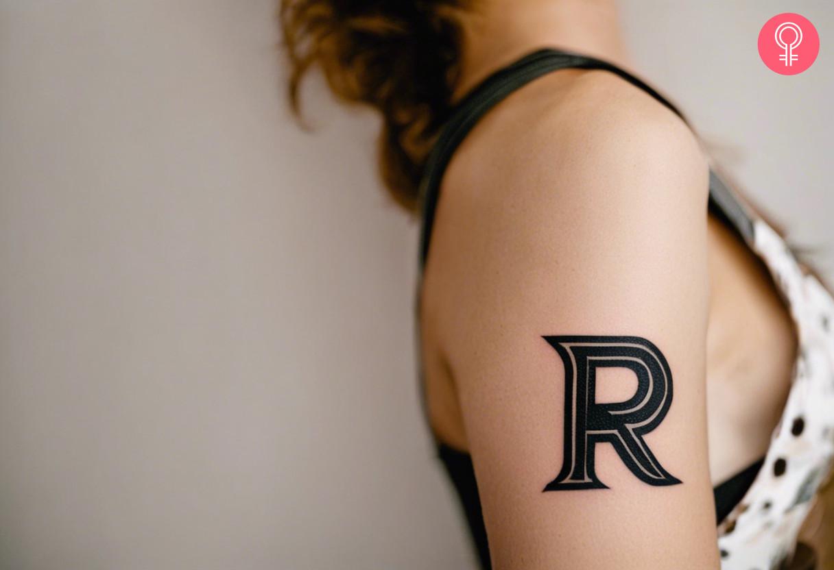 A bold font lettering alphabet tattoo on the upper arm of a woman