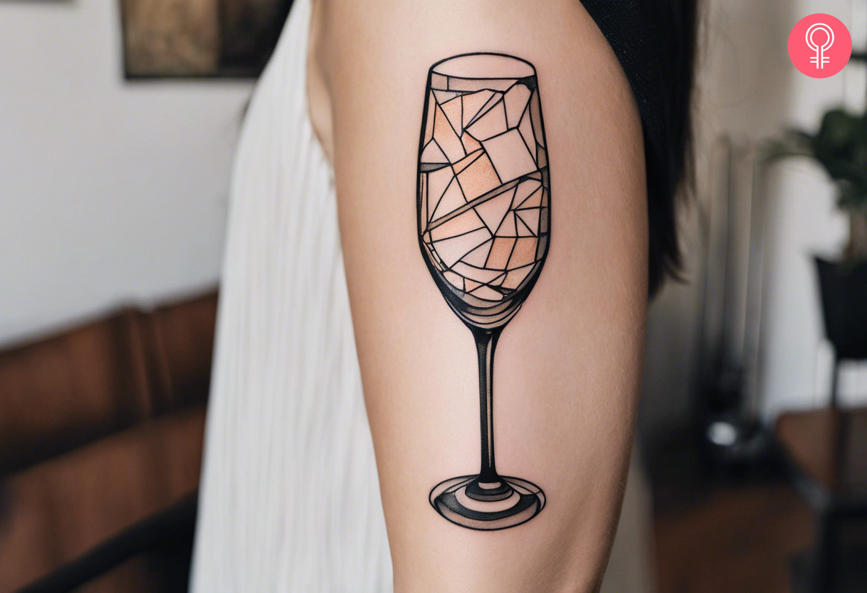 A broken champagne glass tattoo on the upper arm of a woman