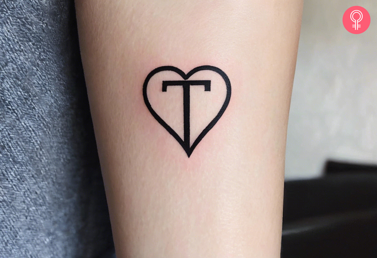 A capital letter T tattoo with a heart on a woman’s forearm