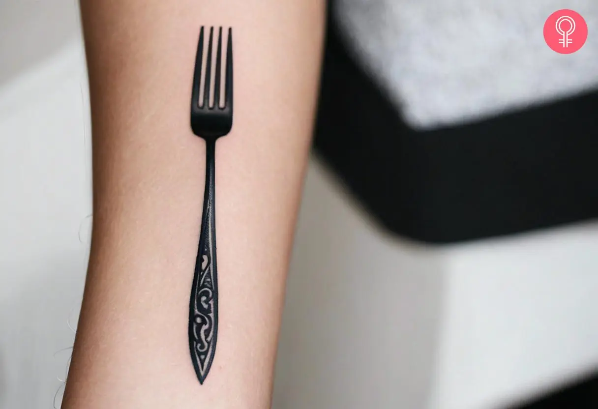 A woman wearing a classic black and gray fork tattoo on the inner arm.