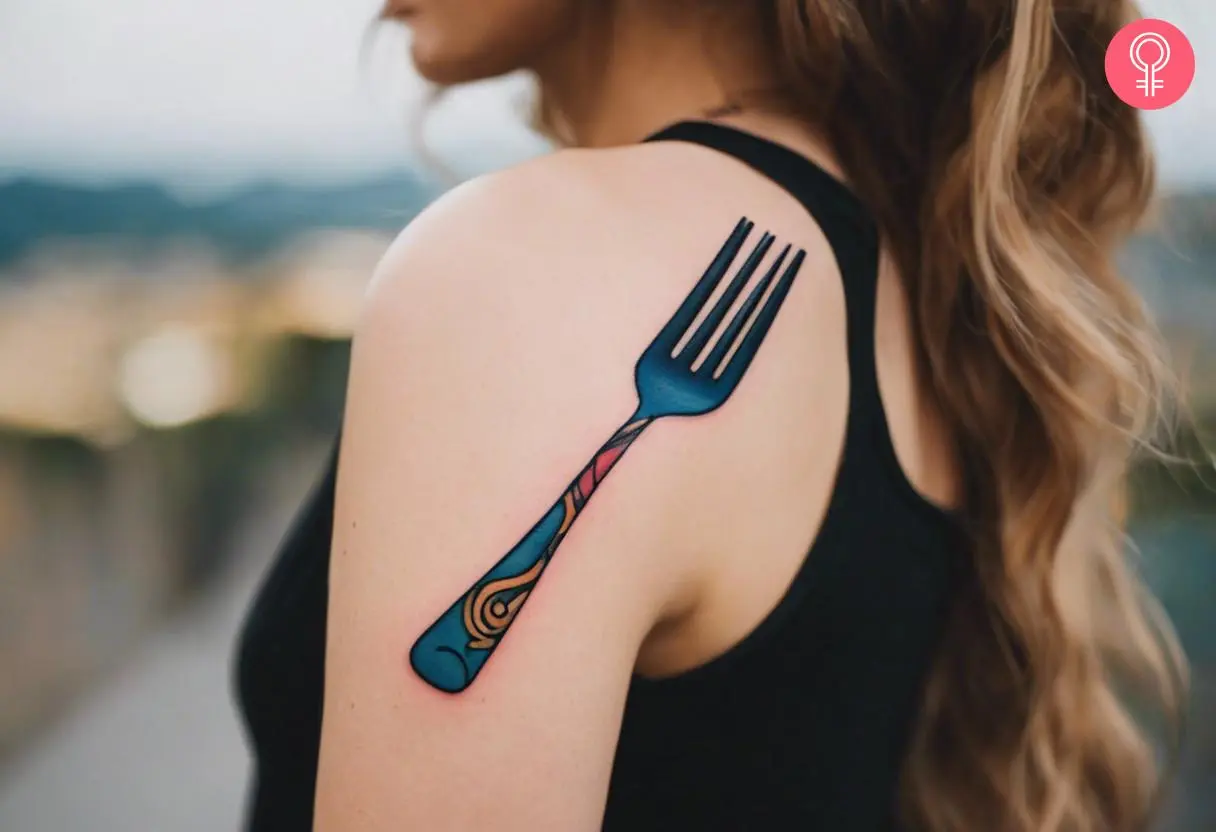 A woman wearing a colorful fork tattoo on the upper portion of the back shoulder