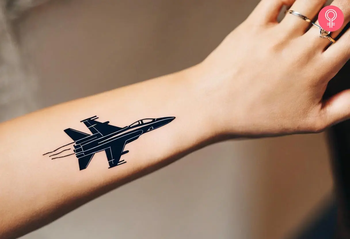 A small and black fighter jet tattoo on the back of the wrist 