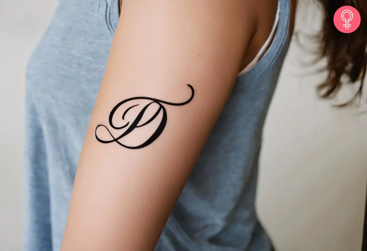 A cursive alphabet tattoo on the upper arm of a woman