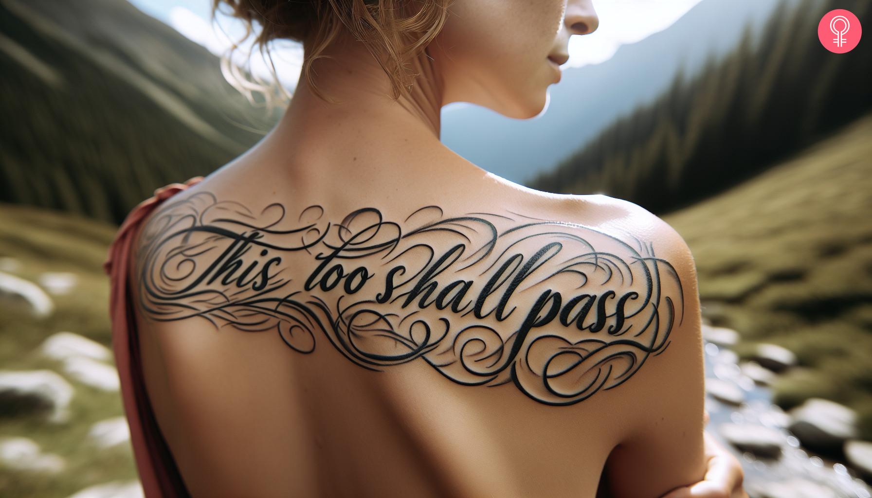 Cursive ‘This Too Shall Pass’ tattoo on a woman’s back