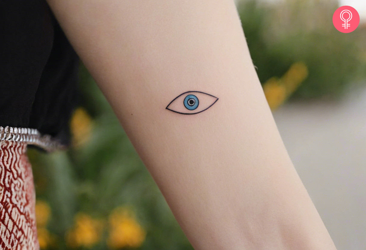 A dainty evil eye tattoo on the forearm of a woman