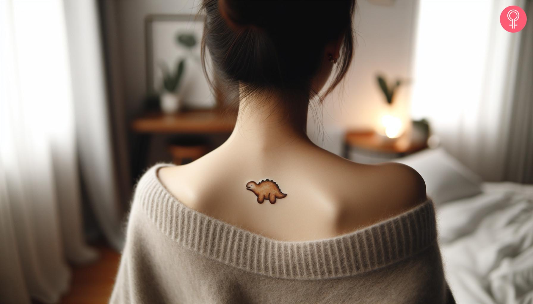 Small dino chicken nugget tattoo on a woman’s upper back