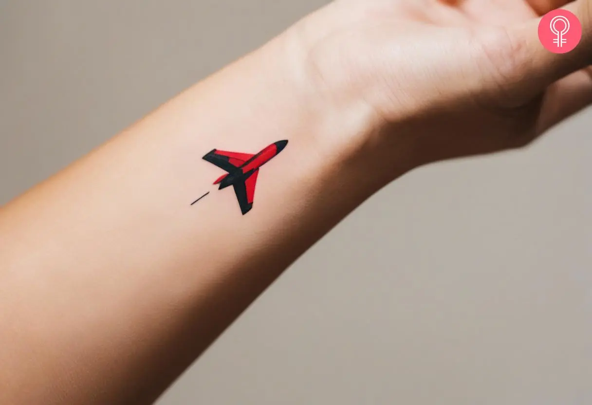 A tiny red and black ink fighter jet tattoo on the wrist