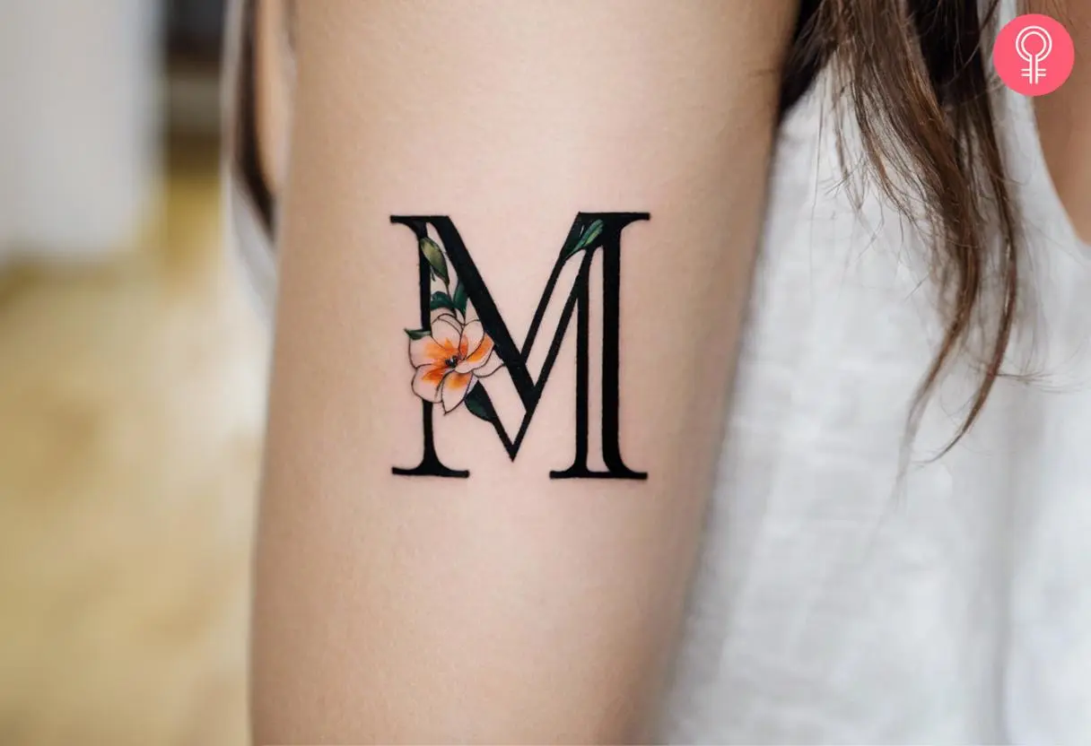 Floral ‘M’ tattoo on the mid-section of the upper arm