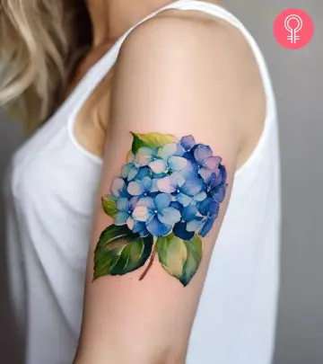 A woman wearing a ‘family birth flower bouquet’ tattoo on the upper arm.