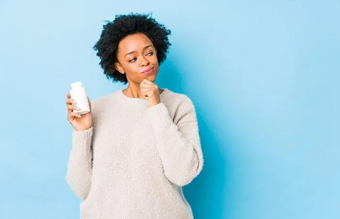 A mid shot of a woman holding a bottle looking sideways with doubtful expression