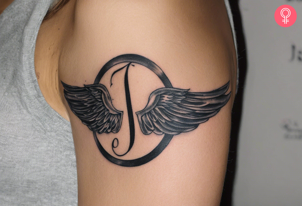 J letter with wings tattoo on the upper arm of a woman