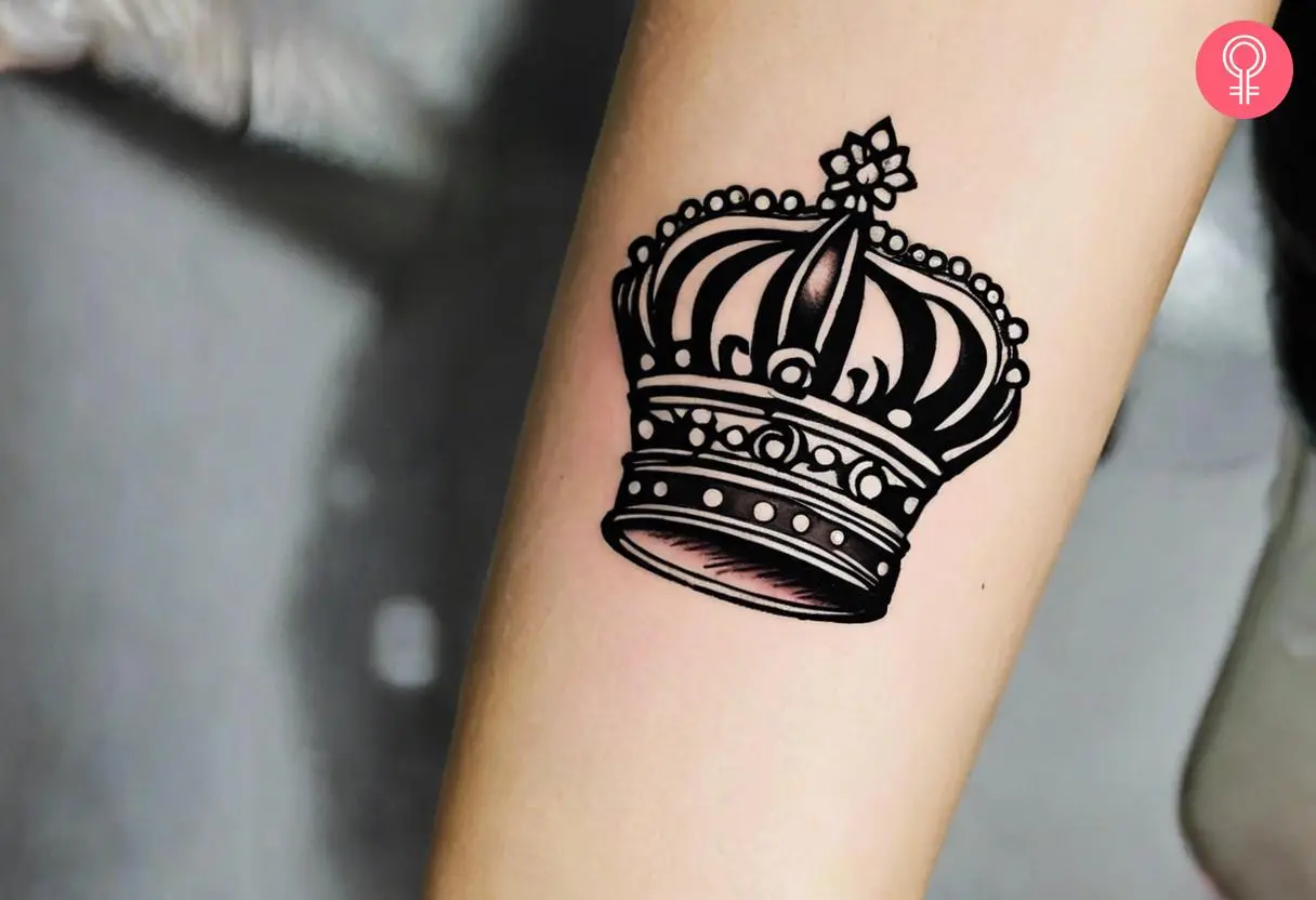 A black ink crown tattoo on the arm of a woman