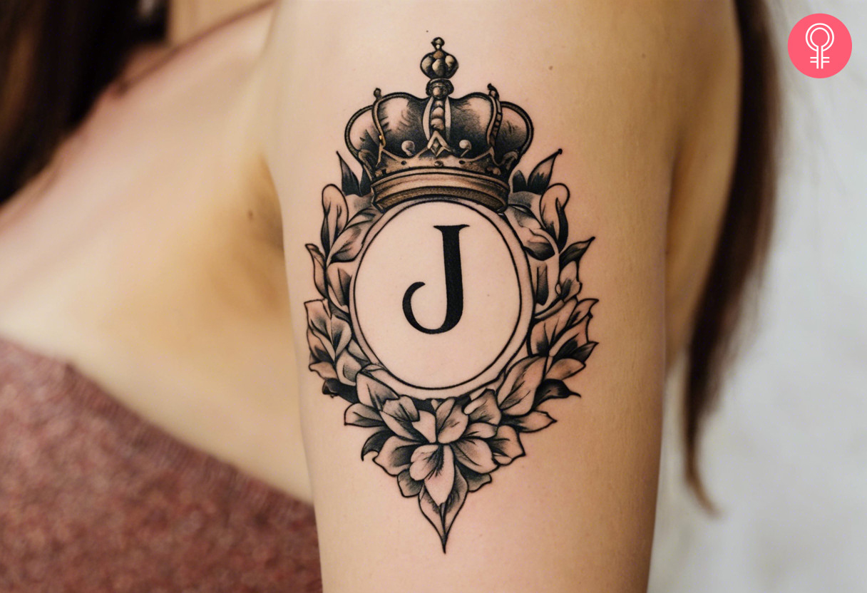 Letter J with crown tattoo on the upper arm of a woman