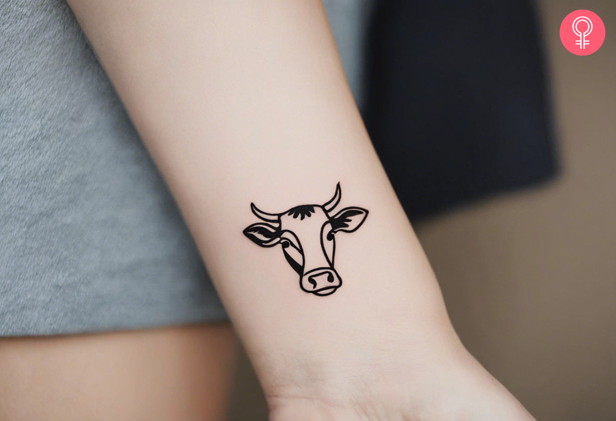 A minimalist cow tattoo on the wrist of a woman