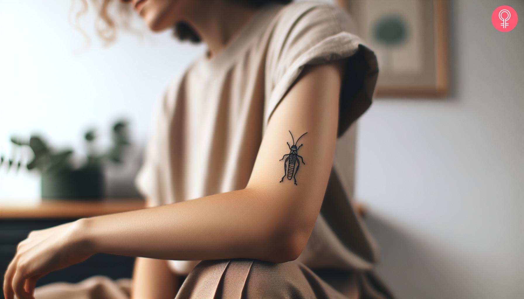 A minimalist grasshopper tattoo on a woman's upper arm