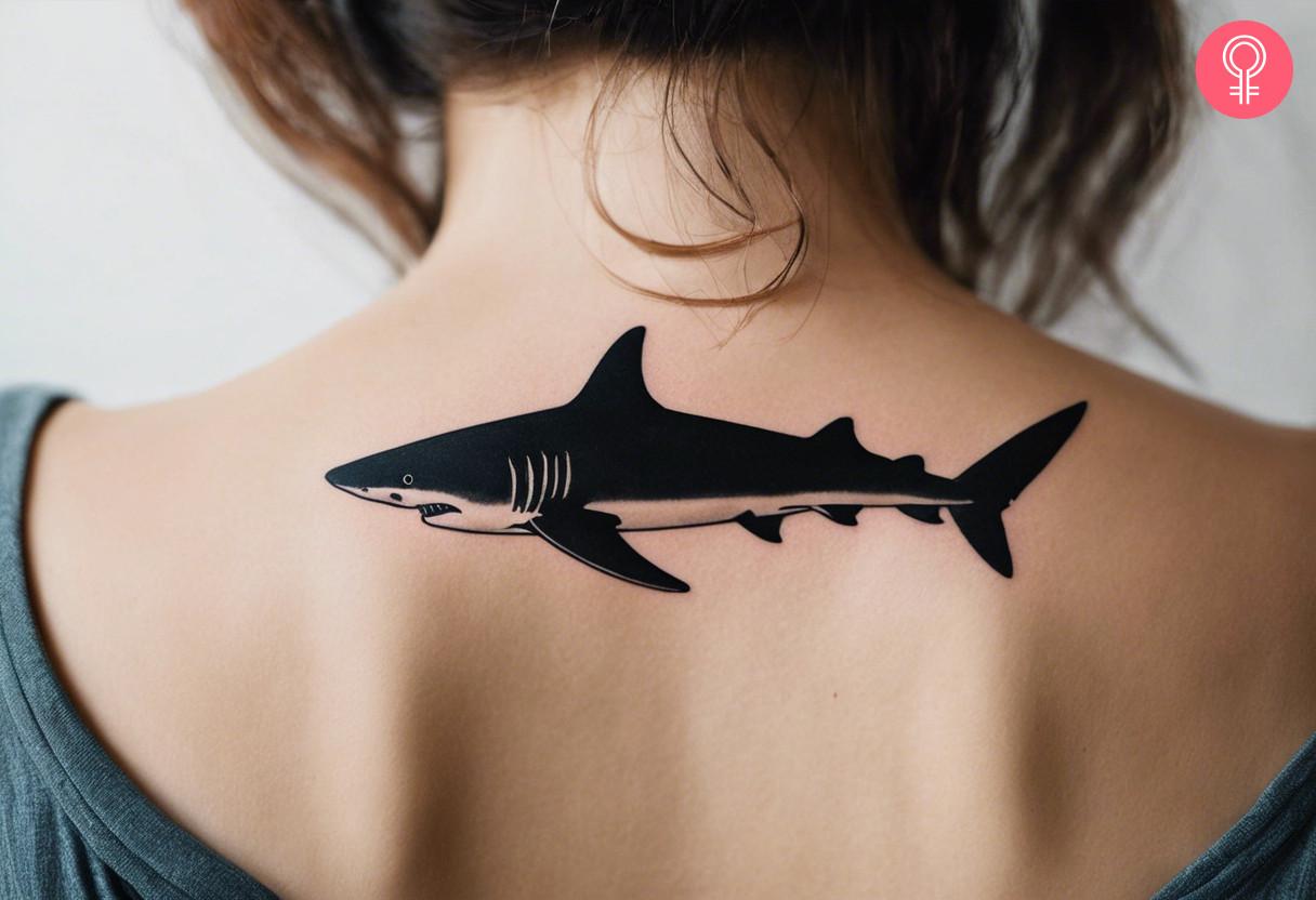 A simple black ink shark tattoo on the upper back