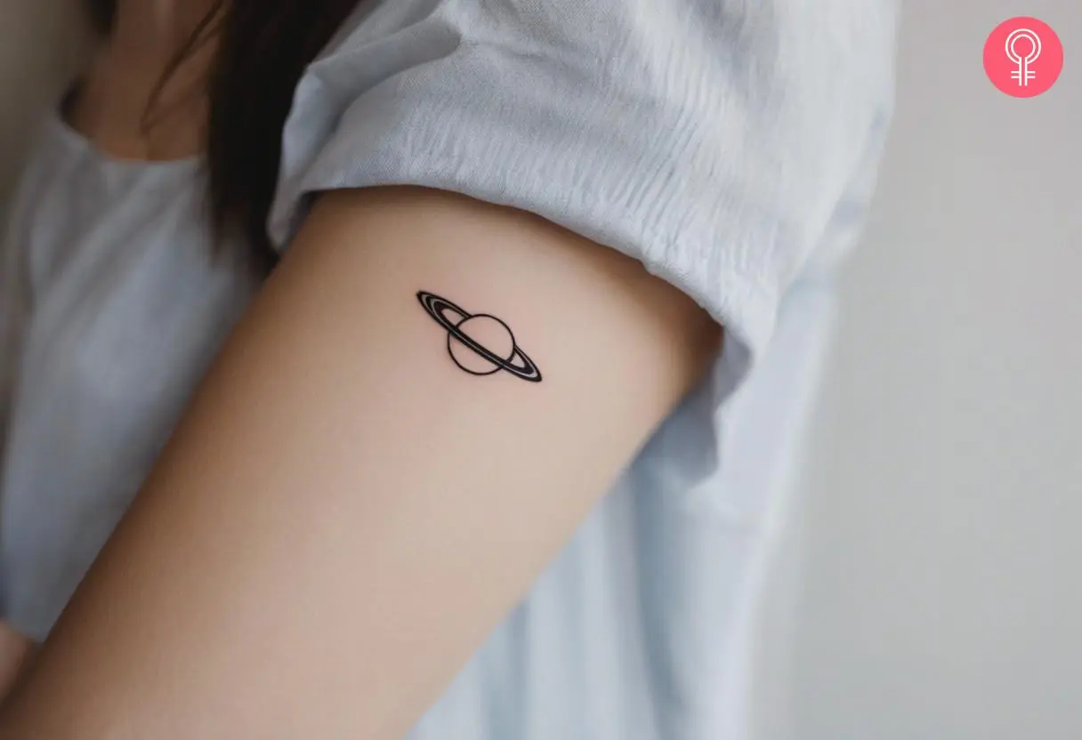 A minimalist saturn tattoo on a woman’s upper arm