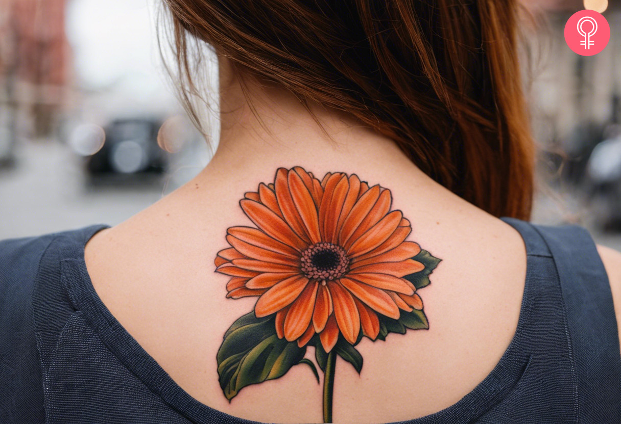 Orange gerbera daisy tattoo on the upper back of a woman