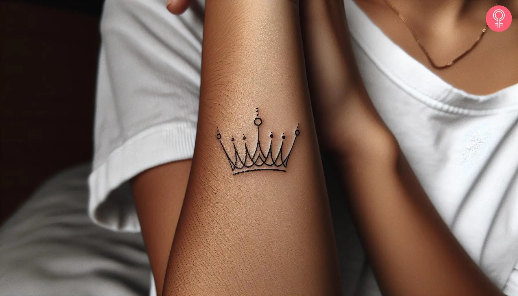 A minimalist black ink crown tattoo on the arm of a woman