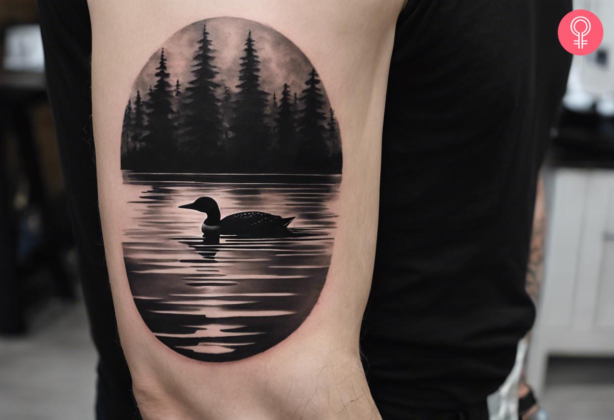 A realistic upper arm tattoo featuring a loon swimming in a lake