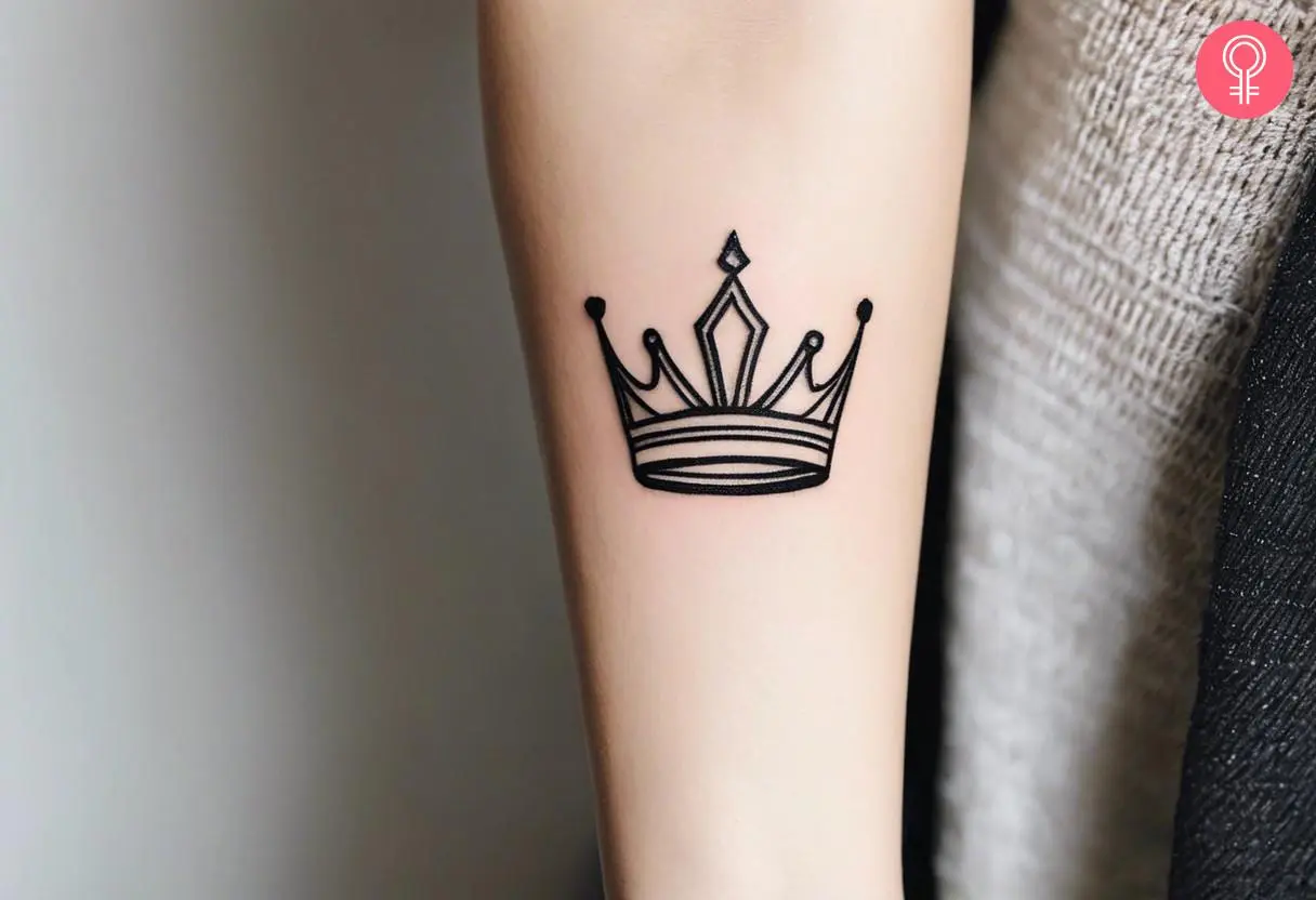 A simple queen crown tattoo on the arm of a woman