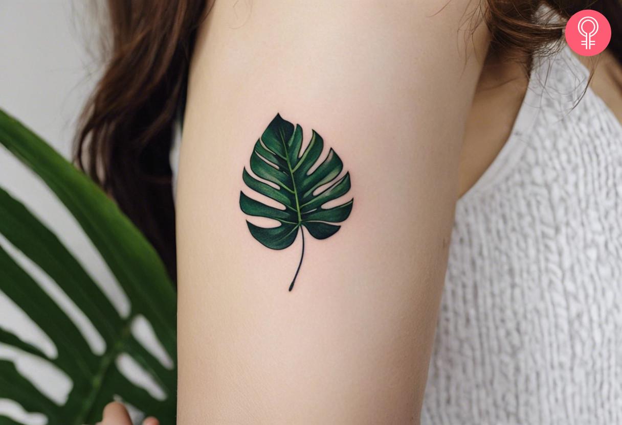 Small Monstera leaf tattoo on a woman’s upper arm