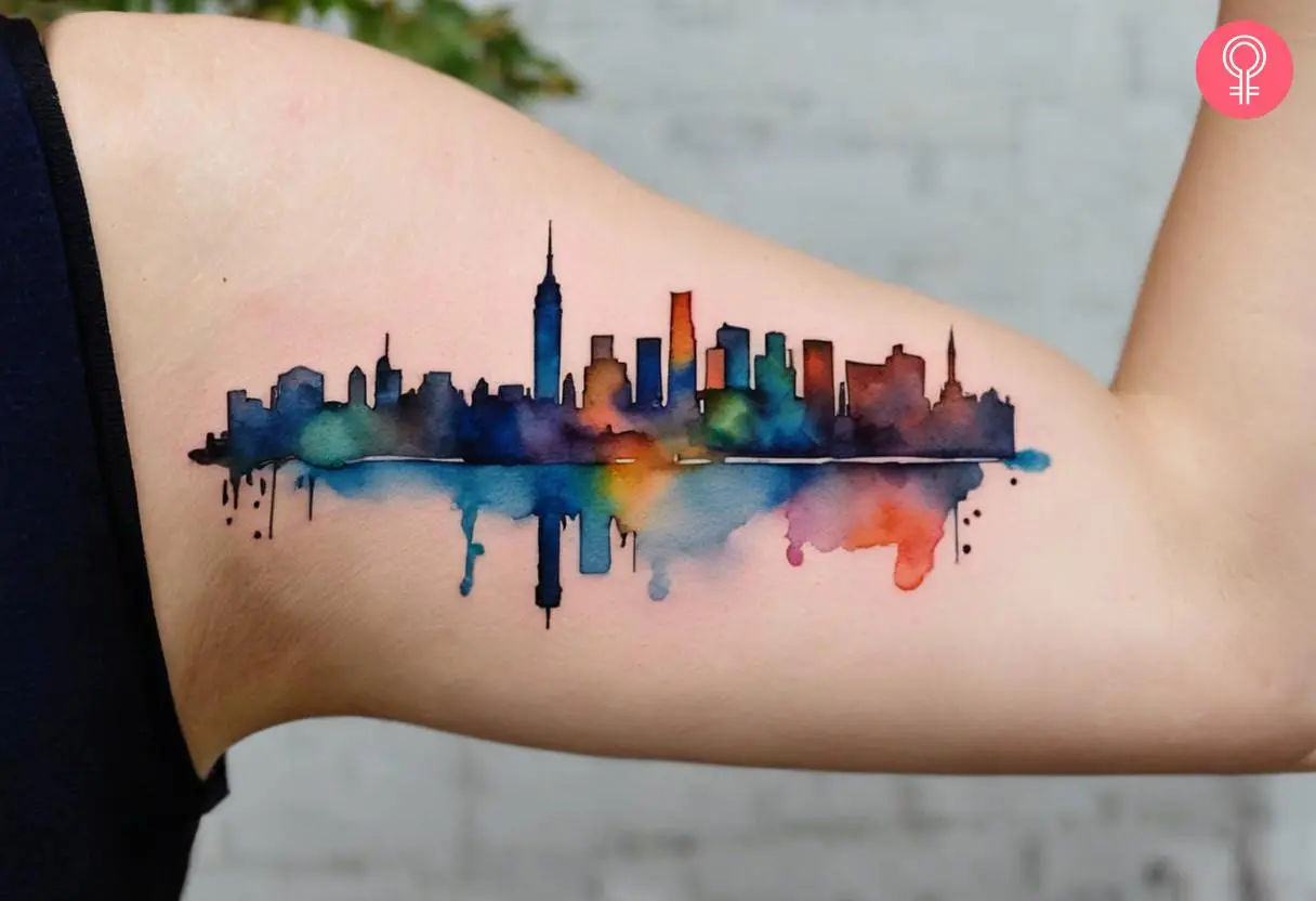 A New York skyline watercolor tattoo on the upper arm of a woman